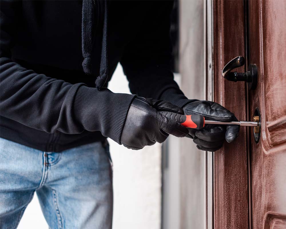 A man breaking into a door with a crowbar, now needing burglary repairs.